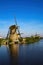 View over dutch water canal on old windmills on green meadow against deep blue cloudless summer sky in rural countryside -