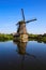 View over dutch water canal on old windmills on green meadow against deep blue cloudless summer sky in rural countryside -