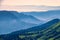 View over the Green Valley, surrounded by high mountains on a pink summer sunset. Layers of mountains in the haze during sunset