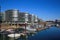 View over marina on modern silver office buildings five boats against blue sky