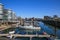 View over marina on modern silver office buildings five boats against blue sky