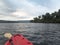 View over the nose of a red plastic canoe boat travelling up River Kong and cutting through the dense jungle