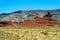 View over plain with green dry grass tufts on red and grey sandstone hill formation butte against blue sky  - Monument Valley