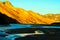 View over riverbed with shallow water and black sand on orange yellow glowing mountain range in the evening sun