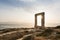 View over ruins of ancient marble doorway monument Portara at sunset in Naxos, Greece.