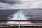 View over stern from upper deck of modern cruise ship showing wake extending into the distance on a grey stormy day in the Tropics