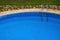 View of a part of the public pool with blue clear water: descent into the pool with perrils, sides, natural stone and grass.