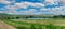 view of pasture with a herd of cows and a pond and agricultural land in late summer