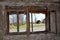 View of paved road and houses from inside of abandoned house through destroyed window with broken window frame mounted on cracked