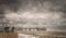 A view of people on a promenade or boardwalk looking at a pier on a stormy day