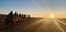 View of people sitting on camels on a road under a blue sky during a beautiful sunrise