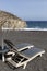 view of Perissa beach on the Greek island of Santorini with sunbeds and umbrellas. Beach is covered with fine black sand, and