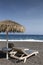 view of Perissa beach on the Greek island of Santorini with sunbeds and umbrellas. Beach is covered with fine black sand, and