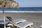 view of Perissa beach on the Greek island of Santorini with sunbeds and umbrellas. Beach is covered with fine black sand, and