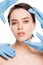 View of plastic surgeons in blue latex gloves touching face of naked girl isolated on white