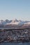 View of the polar town of Tromso in northern Norway and the snowy hills in background at sunset. Orange-red colour lines rocky
