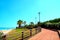 View in Porto Potenza Picena at a wide promenade with bushes, palm trees, light poles and the sea