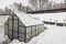 View of a private garden with a snow-covered greenhouse on a chilly winter day.