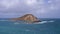 View of Rabbit Island. Waves of Pacific Ocean wash over yellow sand of tropical beach. Magnificent mountains of Hawaiian