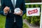 View of realtor holding carton house model and keys near board with sold letters