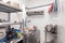 View of restaurant\'s professional washer, sink, brushes, metal shelving and shelves with kitchen utensils, cups, cutting board,