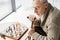 View of retired man in glasses thinking while sitting near chess board at home