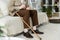 View of retired man holding pill while sitting on sofa near walking cane