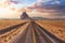 View of a road in a dry desert with a Shiprock mountain peak in the background.