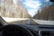 View of the road through the windshield. Snow on the sidelines. Wet asphalt road. Blue sky with clouds. Point of view of the