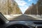 View of the road through the windshield. Snow on the sidelines. Wet asphalt road. Blue sky with clouds. Point of view of the