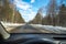 View of the road through the windshield. Snow on the sidelines. Wet asphalt road. Blue sky with clouds. Point of view of the