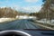 View of the road through the windshield. Snow on the sidelines. Wet asphalt road. Blue sky with clouds. Point of view of the