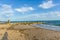 An view of a rocky groyne breakwater with the shadow of the photographer along a sandy beach, choppy blue water and crashing