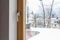 View from the room through a closed balcony window with a handle on a snowy terrace with a wicker chair and a balustrade.