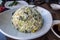 View of a round scoop of vegetable and mushroom fried rice on a small, white plate inside an Asian restaurant