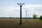 A view of a row of columns of a power line column in a landscape with trees with a field