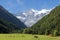 View of Saint Orso meadow and slopes of steep gorge with evergreen pine forest, impregnable granite alpine cliffs. Cogne, Italy