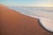 A view of a sandy beach with the tide retreating and a foamy sea