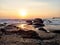 View of the sea with small waves and rocky shore, sunrise reflected in the water