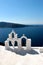 View of sea surface through traditional Greek white church arch with cross and bells in Oia village of Cyclades Island, Santorini,