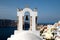 View of sea surface through traditional Greek white church arch with cross and bells in Oia village of Cyclades Island, Santorini,