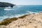 View of sea waves reaching the cliffs and sandy coast of Ponta do Trovao under the blue sky