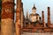 View of a seated Buddha statue among ruined columns in Wat Mahathat, an ancient Buddhist temple in Sukhothai Historical Park