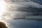 View of the shore of the ocean at low tide. Reflection of the sun in the ocean, surfers in the water.