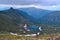 View of small mountain lake in the form of a heart among snowy glaciers, green mountain ranges overgrown with trees, Chersky peak