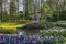 View of small toy windmill near a canal surrounded by blue, violet, yellow, red flowers in Keukenhof park