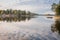 View of the spacious expanse of calm water of large lake, which reflects the sky, coniferous trees along the shore, northern