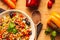 A view of a spelled dish on wooden background with some ingredients around: carrots, peppers, tomatos, parsley and oil