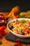 A view of a spelled dish on wooden background with some ingredients around: carrots, peppers, tomatos, parsley and oil