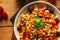 A view of a spelled dish on wooden background with some ingredients around: carrots, peppers, tomatos, parsley and oil